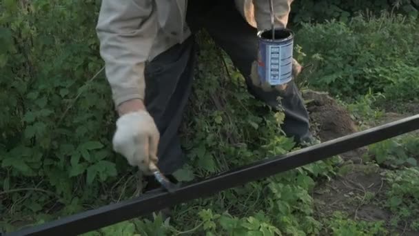 Oude man 70s schildert het ijzeren hek met behulp van een zwarte — Stockvideo