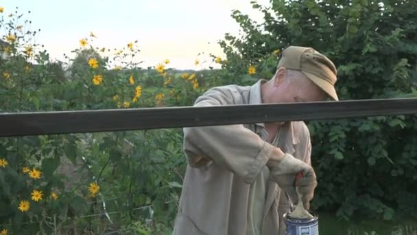 Пожилой мужчина 60-х годов красит железный забор черным — стоковое видео