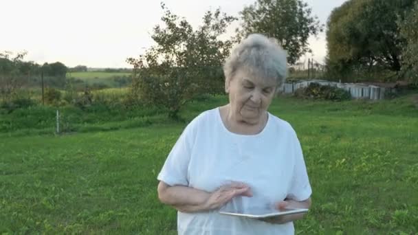 Mujer anciana de 80 años sosteniendo la tableta del ordenador al aire libre — Vídeos de Stock