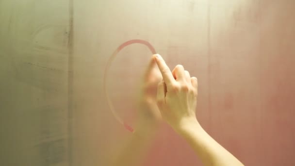 The girl draws a finger drawing a heart on a foggy mirror — Stock Video