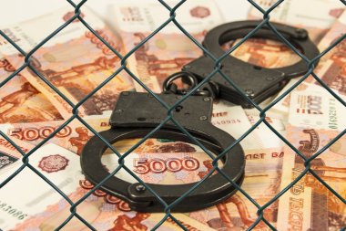 Metal handcuffs on the background of Russian rubles under wire netting (lattice) clipart