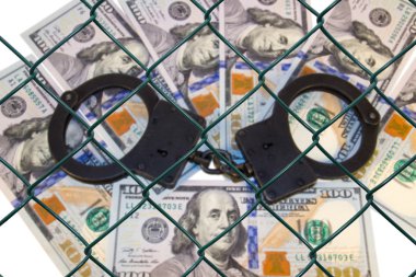 Metal handcuffs on the background of dollars under wire netting (lattice) clipart