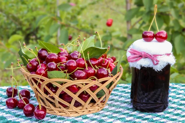 Kosz z czereśni i wiśni jam jar na tle wiśniowego drzewa — Zdjęcie stockowe