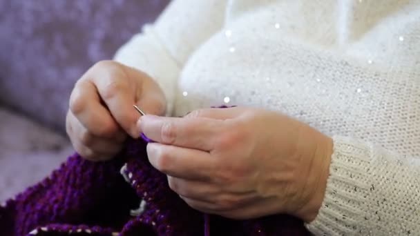 Mulher idosa está sentada no sofá e tricô. Close-up das mãos das mulheres fazendo artesanato handwork, hobby de mulheres adultas no inverno. — Vídeo de Stock
