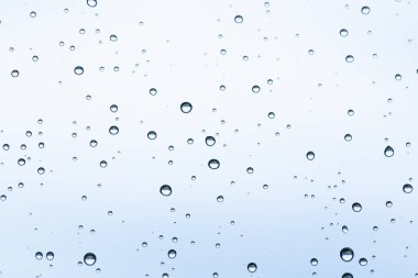 Yağmurlu bir günde açık mavi gökyüzü arkaplanı olan bir pencereye su damlacıklarının makro görüntüsü.
