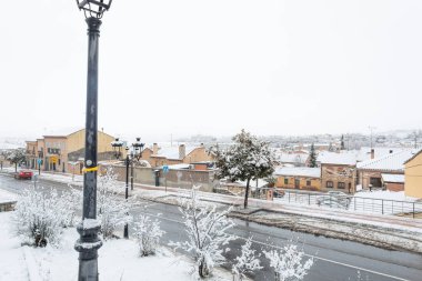 17 Ocak 2026, sakin, karlı bir sabah battaniyesi Avila, İspanya, don kaplı ağaçlar, beyaz çatılar ve tarihi şehre bakan sessiz sokaklar.