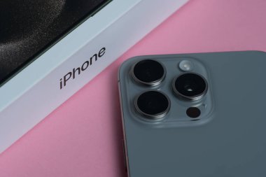 Paketlenmemiş Apple iPhone 15 Pro Max ve 3 kamera, keskin odaklı yumuşak pembe bir arkaplan üzerine kurulmuş.