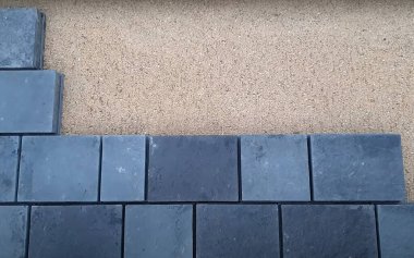 İşçiler bir patika için karanlık taş kaldırımlar döşeyip onları dikkatlice kumdan bir yatağa dizerler. Proje açık havada, açık havada gerçekleşiyor. Doğumda hassasiyet gösteriliyor..