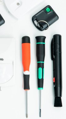 Farklı el aletleri ve eşyalar beyaz bir yüzeye yerleştirilmiştir. Tornavida, kalem ve uzaktan kumanda anahtarı var. Bu sahne kullanıma hazır araçlarla bir çalışma alanı gösterir.