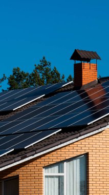 Güneş panelleri tuğla bir evin çatısını kaplıyor. Yandan yükselen bir baca, berrak mavi bir gökyüzü tarafından çerçevelenir. Ayarlar, modern enerji ve geleneksel mimari dengesini gösteriyor..