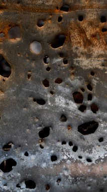 Birçok deliği olan metal bir yüzeye yakından bak. Metalde pas ve aşınma izleri var. Işık yüzeyden yansıyor. Bu sahne, maddenin zamanla bozulmasını görüntüler..