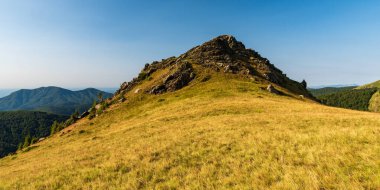 Zirvede kaya oluşumuyla kaplı çayırla kaplı tepe ve arka planda diğer tepeler - Romanya 'nın Valcan dağlarındaki Oslea dağ sırtı
