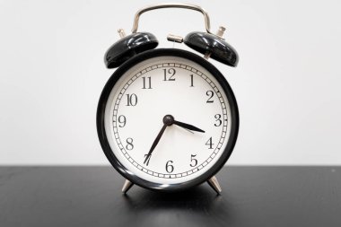 Ofis Masasında Zaman Yönetimi Konsepti için klasik Siyah Alarm Saati. Sabah rutinlerini, teslim tarihlerini, verimliliği ve profesyonel bir çalışma ortamında dakikliğin önemini sembolize eder..