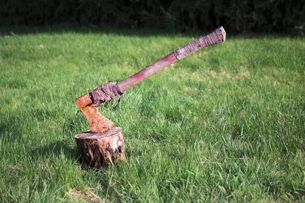 Ржавый топор застрял в блоке, изолированном на траве — стоковое фото