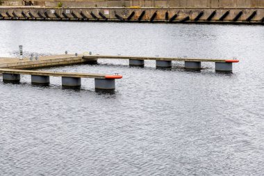 Arka planda beton bir set ile sakin gri suya uzanan, modern, boş, yüzen ahşap rıhtım bölümü geniş görünüm.