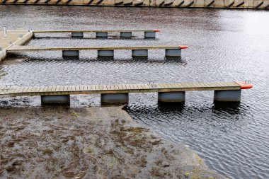 Karanlık su üzerinde uzanan üç paralel ahşap duba veya rıhtım çekim, altında bulanık alg kaplı su bir bölüm.