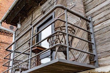 Kapüşonlu mavi ceketli bir adamın, beton bir iskelede küçük bir sandalyede balık tutarken, gri bir savaş gemisinin kıç tarafının önünde çekilmiş yakın plan fotoğrafı..