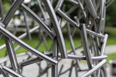 Karmaşık, soyut, parlak, gümüş krom metal tüplerden yapılmış, kaotik, açısal ve iç içe geçmiş bir heykelin aşırı yakın çekimi..