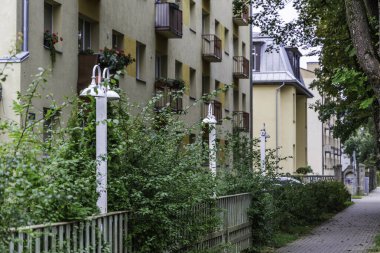 Modern sokak ışıkları ve yeşil çalılar birçok balkonu olan bir apartmanın yanında asfalt kaldırım hizasında..