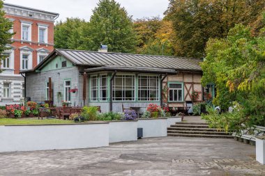 Yeşil çatılı, büyük pencereli ve çiçeklerle çevrili yenilenmiş ahşap bir kafe ya da restoran binası..