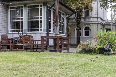 Kafenin dışındaki ahşap masa ve sandalyelerin alçak açılı görüntüsü. Zarif tarihi bir binanın yanında, çimen ön planda..