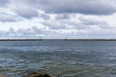 Kargo kanalı girişinde geniş bir perspektif var. Ters dalgalanan sularda yeşil ve kırmızı navigasyon ışıkları var. Dalgalı suyu dramatik ve çalkantılı gökyüzünden ayırıyor..