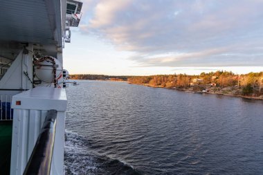 Bir yolcu gemisinin yan güvertesinden geniş açı görüntüsü, geminin korkuluklarını ve İskandinav takımadalarının geçişini gösteriyor..
