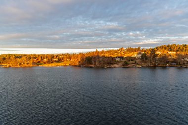 Karanlık suların ötesinden İskandinav takımadalarının yoğun ormanlık ve meskun kıyı şeridine doğru geniş bir görüş açısı var..