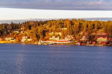 Yoğun yerleşik İskandinav kıyı şeridinin panoramik manzarasında sıcak güneş ışığı altında daha geniş, muhtemelen ticari ve ticari binaların karışımı yer alıyor..