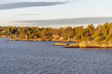 Geleneksel kırmızı ve beyaz evlerin bulunduğu kayalık, ormanlık bir kıyı şeridi İskandinav takımadalarının rahat ve kırsal yaşam tarzını somutlaştırıyor..