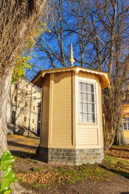 Stockholm 'de açık mavi bir gökyüzünün altında ağaçlarla çevrili, taş tabanı ve penceresi olan tuhaf, küçük, sarı ahşap bir pavyon..