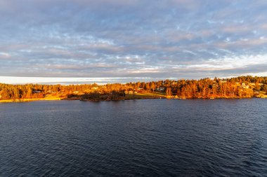 Karanlık suların ötesinden İskandinav takımadalarının yoğun ormanlık ve meskun kıyı şeridine doğru geniş bir görüş açısı var..