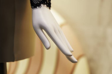 Siyah dantelli bir kol manşeti olan beyaz bir mankenin yakın çekimi, geniş, bulanık, açık pembe / bej bir vitrinde sergileniyor..