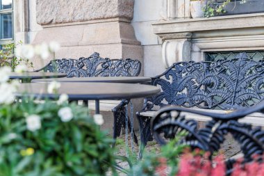 Siyah işlenmiş demirden bir kafeterya tezgahı ve masasının eğreltiotu yaprağı desenine yakın plan, bulanık ön planda çiçekler.