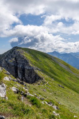 Bir grup insan bulutlu bir gökyüzünün altındaki dik yeşil bir dağ sırtında yürüyor. Tatras 'ta macera, sağlıklı yaşam tarzı ve yaz turizmi kavramı.
