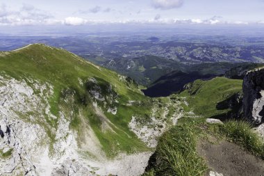 Küçük bir kasabası olan yeşil bir vadiye uzanan dik kayalık bir yamacın yüksek açılı görüntüsü. Ölçek, mesafe ve gayrimenkul konumu kavramı.