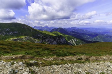 High altitude mountain ridge featuring steep rocky cliffs and lush green slopes under a cloudy sky. Perfect for outdoor adventure and travel themes.