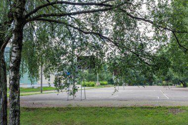 Bir parkta ya da huş ağacı yapraklarıyla çerçevelenmiş okul bahçesinde boş bir basketbol sahası. Eğlence, spor ve toplum etkinliği için şehir spor altyapısı.