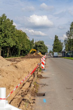 Sarı kazıcı, güvenlik engelleri olan bir şehir caddesi tamirhanesinde çalışıyor. Belediye mühendisliği kavramı, kamu hizmetleri güncellemeleri ve kentsel kalkınma.