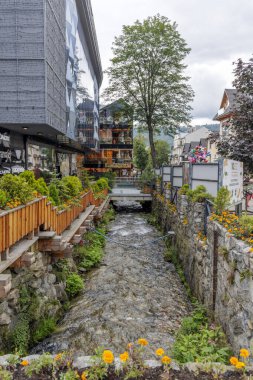 Hızla akan bir dağ deresi alışveriş merkezleri, çiçekler ve modern cam mimarisi olan bir şehir merkezinden geçiyor..