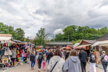 Turistlerle, hediyelik eşya tezgahlarıyla ve dağlık bir tatil köyünde bulutlu bir gökyüzünün altında alışveriş yapan kalabalık bir açık hava pazarının geniş bir görüntüsü..