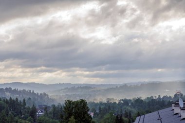 Uzak dağ sırtları ve gri bulutların arasından süzülen yumuşak güneş ışığıyla sisli bir vadinin atmosferik görüntüsü..