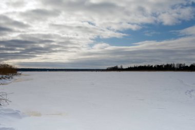 Uçsuz bucaksız donmuş bir gölde bulutlu bir kış gökyüzünün altında buzda balık tutan insanların uzak görüntüsü. Yerel gelenekleri ve mevsimsel açık hava aktivitelerini yakalar.
