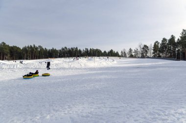 İnsanlar kış etkinliklerinin keyfini çıkarıyor ve gündüz vakti eğlence parkında renkli lastik tüplerle karlı bir tepeden kayıyorlar..