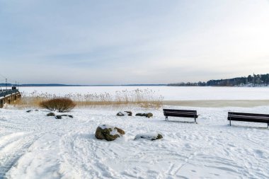 Geniş, karla kaplı donmuş göle bakan ahşap park bankları berrak bir kış gökyüzünün altında..