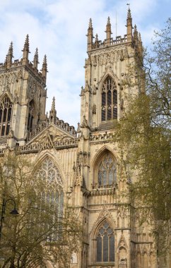 İngiltere 'deki York Minster' ın Gotik katedral kulelerinin detaylı görüntüsü. Karmaşık oymalar ve ağaçlarla çevrili kavisli pencereler ve berrak gökyüzü..
