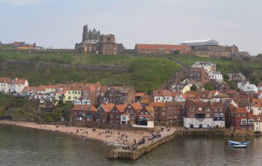 İngiltere 'de Whitby: Kırmızı çatılı evleri, bir plajı ve bir tepenin üzerindeki tarihi kalıntıları olan kıyı kasabasının manzaralı manzarası.