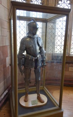 İngiltere 'de Yorkshire: Büyük pencereleri ve taş duvarları olan tarihi bir binanın içinde cam bir kutuda sergilenen ortaçağ şövalye zırhı.