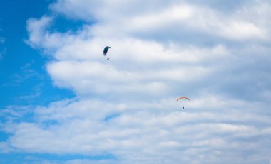 Parçalı bulutlu gökyüzünde süzülen iki paraşütçü açık hava sporları ve maceraların güzelliğini yakalıyor..