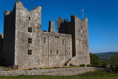 Bolton Şatosu - İngiltere: Uzun kuleleri ve dar pencereleri olan eski, iyi korunmuş bir taş kale parlak mavi bir gökyüzünün altında duruyor.